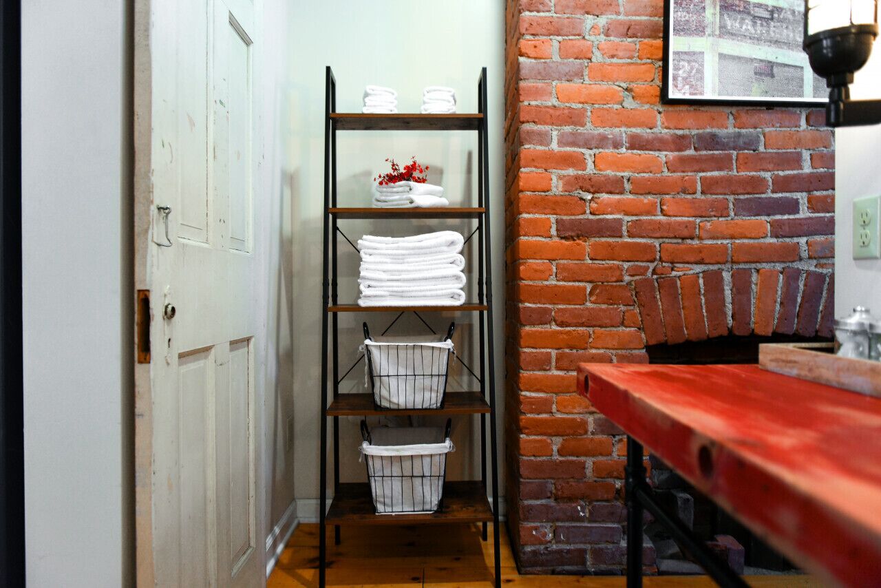 A hallway with a white door, a metal shelf with towels and baskets, a brick wall, and a red bench.