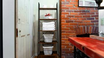 A hallway with a white door, a metal shelf with towels and baskets, a brick wall, and a red bench.