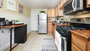 A modern kitchen with wooden cabinets, stainless steel appliances, a black countertop, and a patterned rug. - 1210 James St. #2 · Free Off Street Parking! (Pittsburgh)