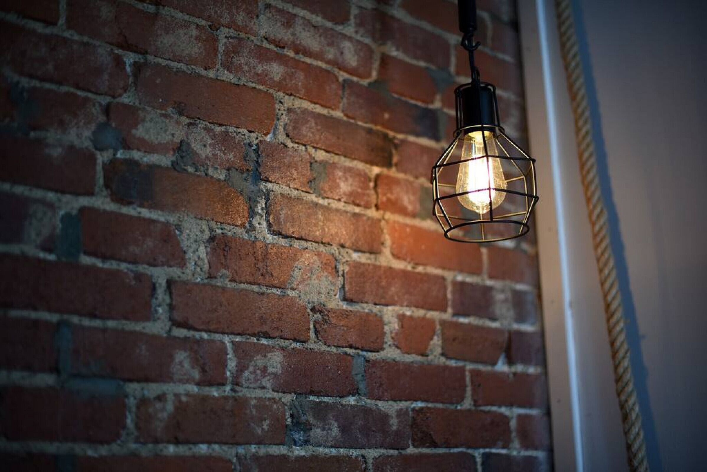 En hängande lampa med en synlig glödlampa, placerad framför en tegelvägg.