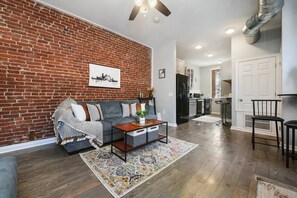A living room with a brick wall, a sofa, a coffee table, and a rug. - Bright & Stylish Apartment with King Bed & Parking (Pittsburgh)
