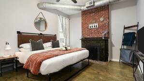 Un dormitorio con cama, mesita de noche, espejo, chimenea y ventilador de techo.