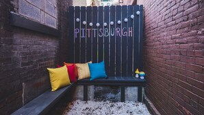Un banco con cojines de colores en un callejón con una pared de ladrillo y una valla de madera con la palabra 'Pittsburgh'.