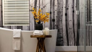 Un espace de détente avec une baignoire aux formes arrondies, une petite table en bois agrémentée de serviettes et de bougies, et un vase rempli de fleurs jaunes.