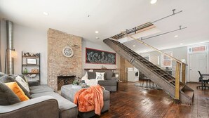 A spacious living room with a brick wall, a fireplace, a staircase, and a modern staircase. - 1207 Ocala - Boat House - North Side (Pittsburgh)