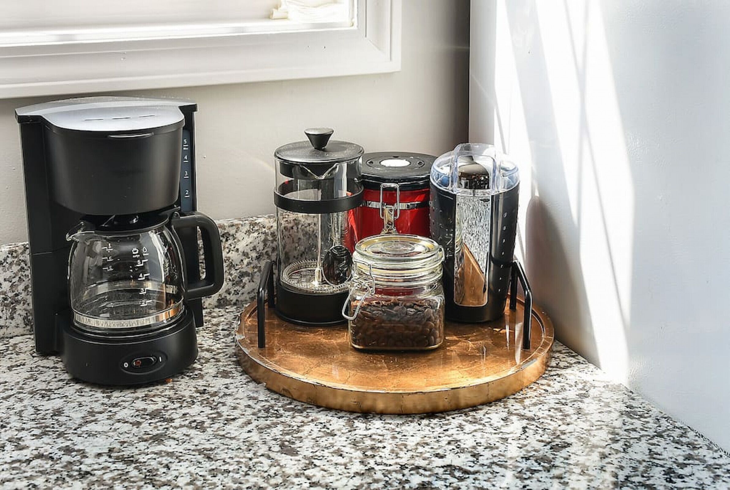 A coffee maker, a grinder, and a jar of coffee beans on a kitchen counter.
