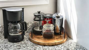 A coffee maker, a grinder, and a jar of coffee beans on a kitchen counter.