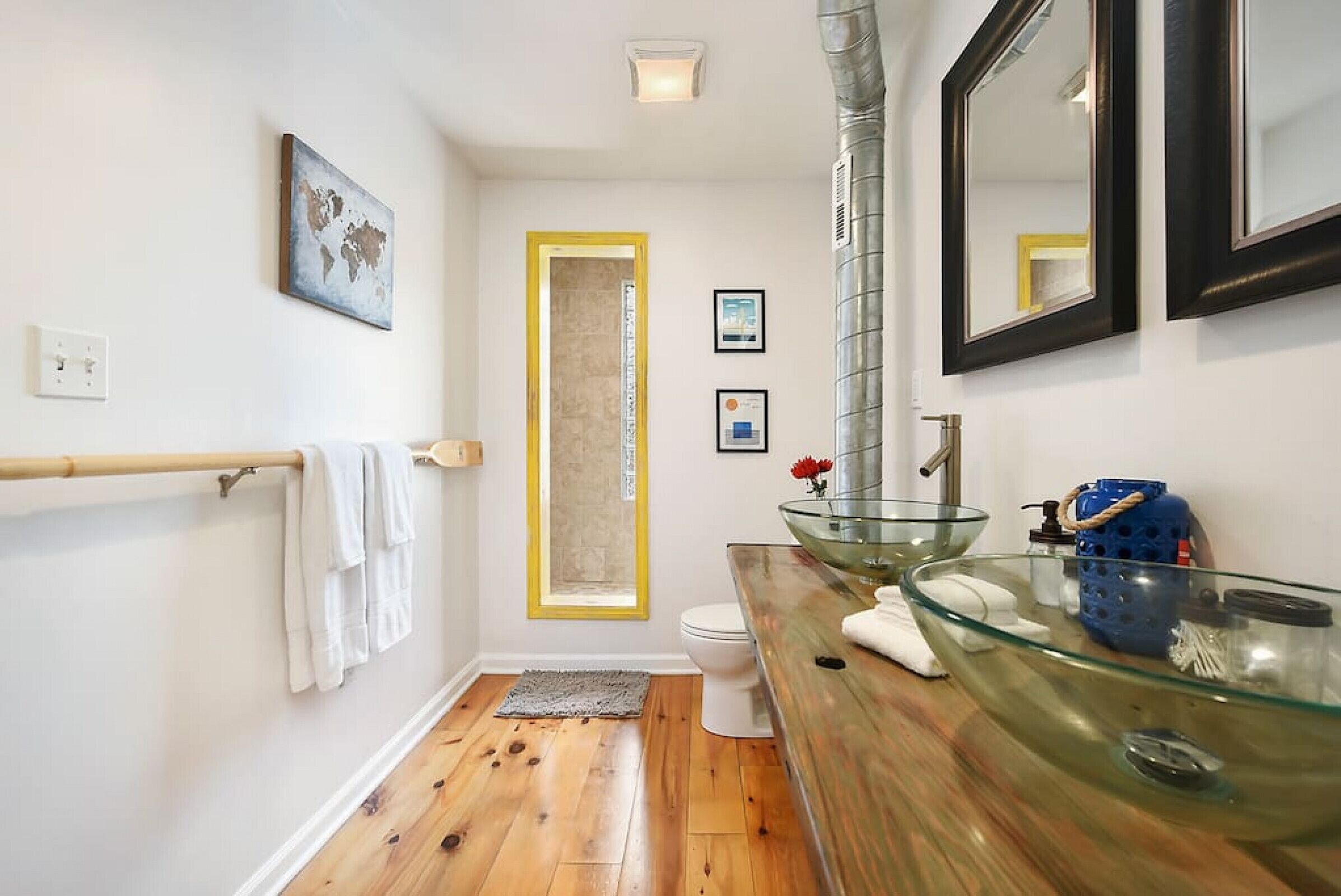 Un baño con lavabo de cristal, suelo de madera y un perchero para toallas.