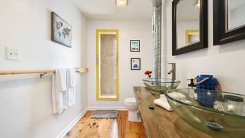 Un baño con lavabo de cristal, suelo de madera y un perchero para toallas.