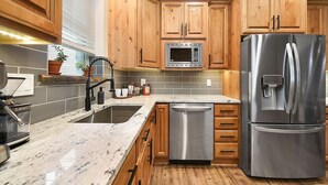 A kitchen with wooden cabinets, a stainless steel refrigerator, a dishwasher, a microwave, and a granite countertop. - 190.5 44th St. - Lawrenceville (Pittsburgh)