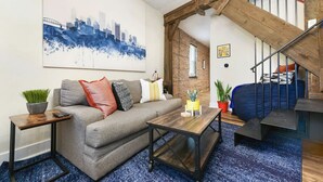 A living room with a sofa, coffee table, and a cityscape painting. - 190.5 44th St. - Lawrenceville (Pittsburgh)