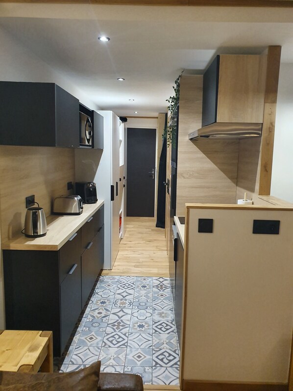 A compact kitchen with modern appliances, a patterned tile floor, and a small wooden table.
