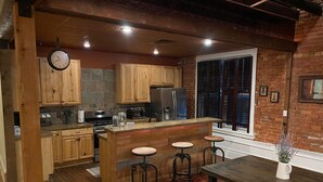 A kitchen with wooden cabinets, a central island with stools, a refrigerator, and a window with blinds.