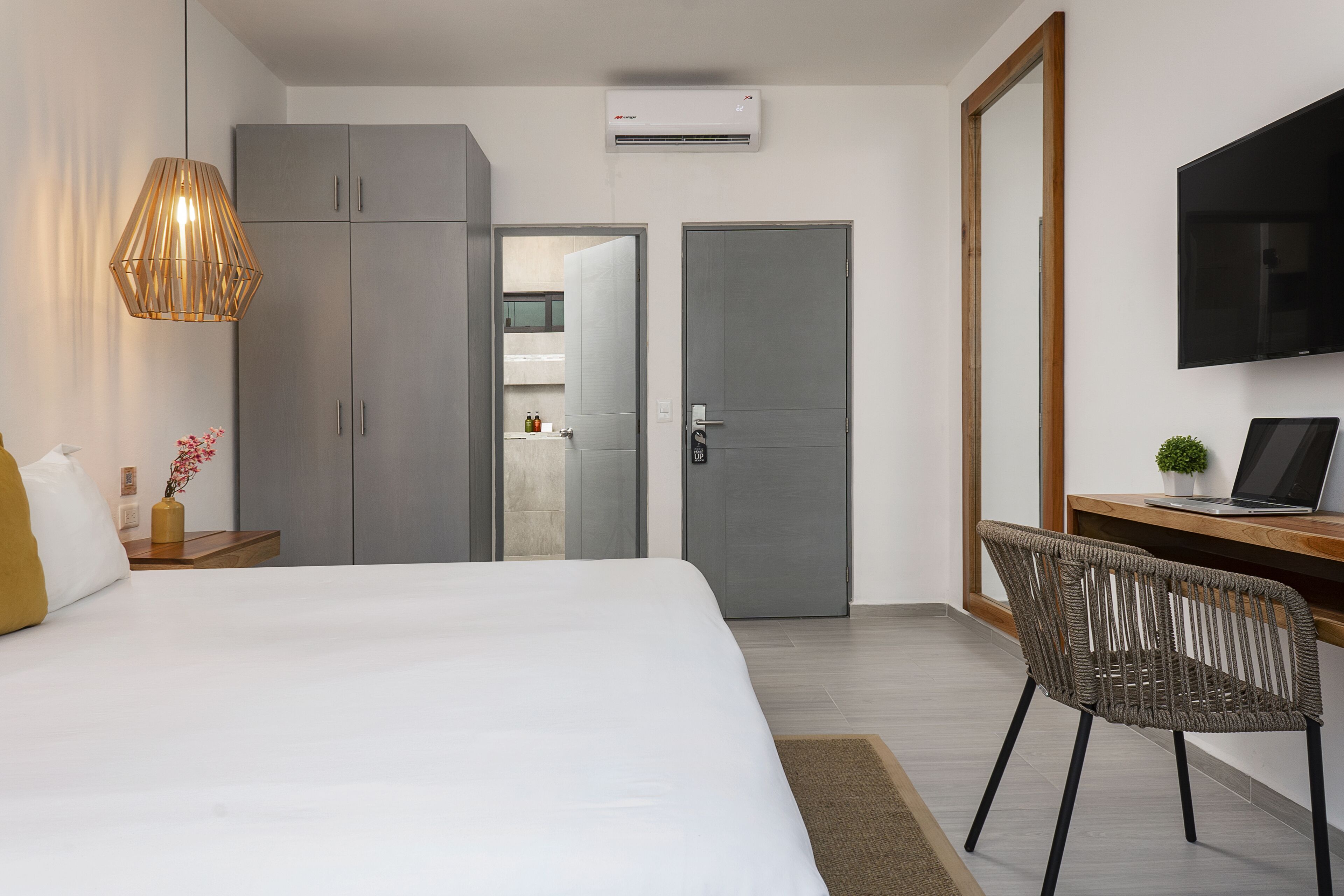 A modern hotel room with a large bed, a desk with a laptop, a television, and a wardrobe.
