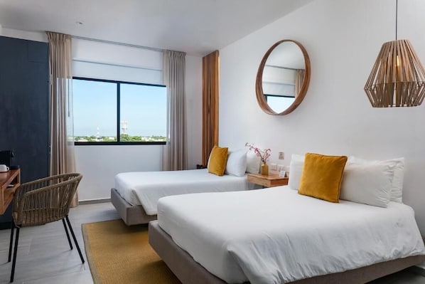 Habitación de hotel con dos camas, un escritorio, una silla, un ventanal con vistas, un espejo y una lámpara colgante.