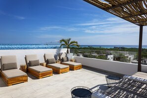 A rooftop terrace with wooden lounge chairs, a round table, and a view of the sea.