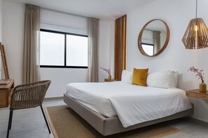 A modern bedroom with a large bed, a wooden side table, a chair, and a window with curtains.