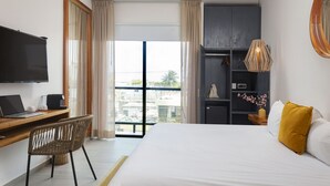 Habitación de hotel con cama, escritorio, computadora portátil, televisión y ventana grande con cortinas.
