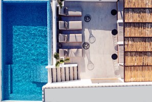 Vue aérienne d’un espace piscine sur le toit, avec des chaises longues, une petite table et une zone couverte de chaume.