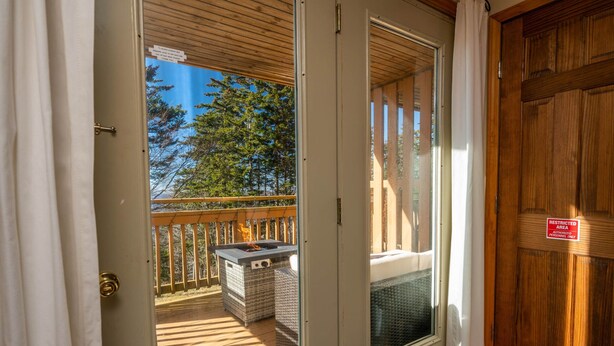 A wooden door with a "RESTRICTED AREA" sign, a balcony with a fire pit, wicker furniture, and a view of trees. - Cozy Condo at Summit- 103D (Snowshoe)