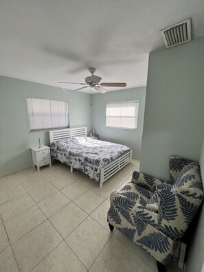 A bedroom with a bed, a nightstand, a chair, a ceiling fan, and two windows. - Bungalow oasis with lots of room (Big Pine Key)