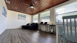 Une pièce spacieuse avec un plafond en bois, un canapé d’angle noir, une petite table et un bureau avec deux ordinateurs portables.