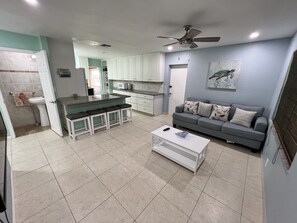 A modern kitchen with white cabinets, a central island with bar stools, a grey sofa with patterned cushions, and a ceiling fan. - Bungalow oasis with lots of room (Big Pine Key)
