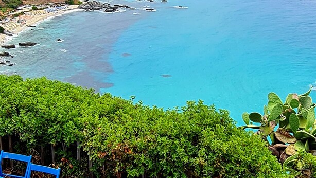 A coastal view with a table and chairs in the foreground, a rocky shoreline, and a distant town on the hills. - Top location - tranquillity - pool - garden & sea view (Zambrone)