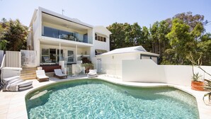 Una moderna casa a due piani con piscina, area salotto esterna e patio coperto.