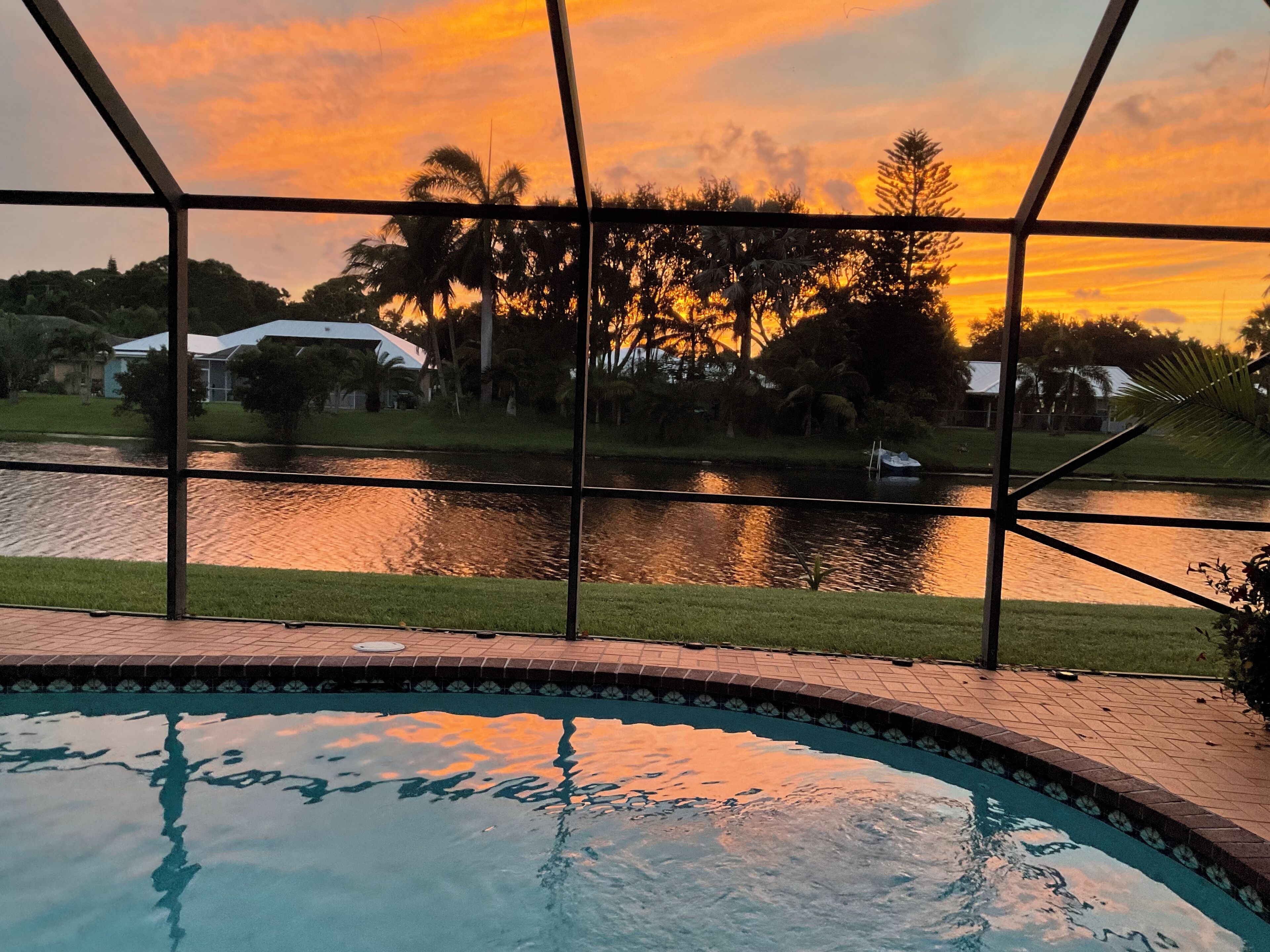 Une piscine avec vue sur un lac et des arbres, au coucher du soleil.