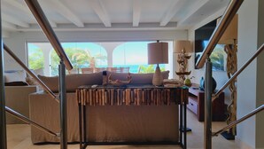 Ein geräumiges Schlafzimmer mit einem großen Bett, einem Holz-Kopfteil und Meerblick durch große Fenster.