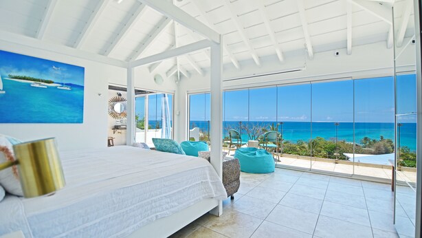 Ein geräumiges Schlafzimmer mit einem großen Bett, Blick auf das Meer und einem Balkon mit Sitzgelegenheit.