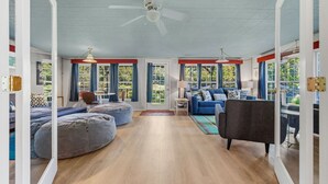 A spacious living room with a ceiling fan, a blue sofa, a grey bean bag, and a wooden floor. - Waterfront! Firepit~3 King bedrms~playroom~kayaks~near restaurants (Hot Springs)
