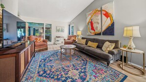 A modern living room with a large sofa, a coffee table, and a TV. There are two lamps and a rug on the floor. - Waterfront! Firepit~3 King bedrms~playroom~kayaks~near restaurants (Hot Springs)