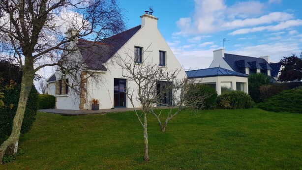 A white house with a sloped roof and a chimney, surrounded by a well-maintained lawn and trees.