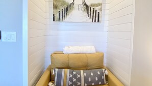 A cozy room with a yellow sofa, a patterned pillow, and a framed beach pathway artwork on the wall.