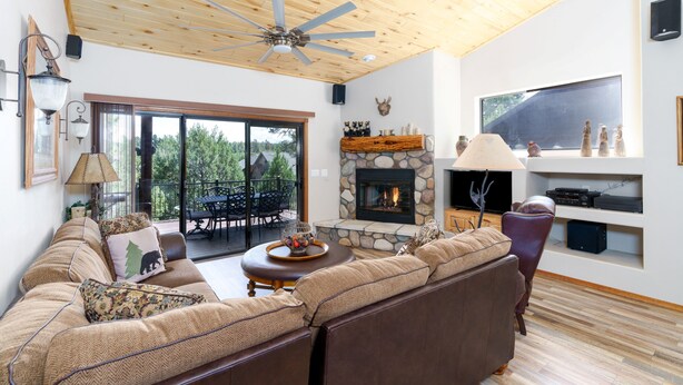 Una sala de estar acogedora con chimenea de piedra, techo de madera y un amplio ventanal con vistas a una terraza.