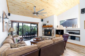 Una sala de estar acogedora con chimenea de piedra, techo de madera y un amplio ventanal con vistas a una terraza.