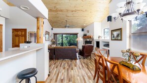 Un espacio habitable amplio con techo de madera, una mesa de comedor con sillas, un sofá y una zona de cocina con barra y taburetes.