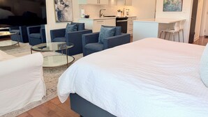 Una sala moderna con una cama grande, sofás, una mesa de centro de vidrio, televisión y una cocina con armarios y estufa.