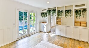 A spacious room with a wooden floor, white walls, and a large window with a view of greenery outside.