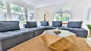 Una sala moderna con un sofá modular, una mesa de centro de madera y ventanas amplias.