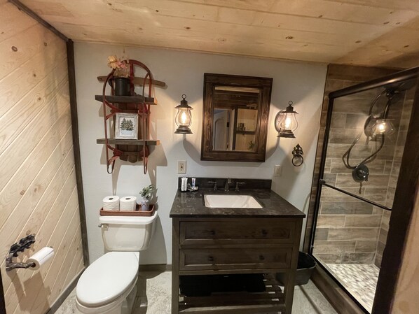 A bathroom with a wooden vanity, a toilet, a shower with glass doors, and wall-mounted sconces.