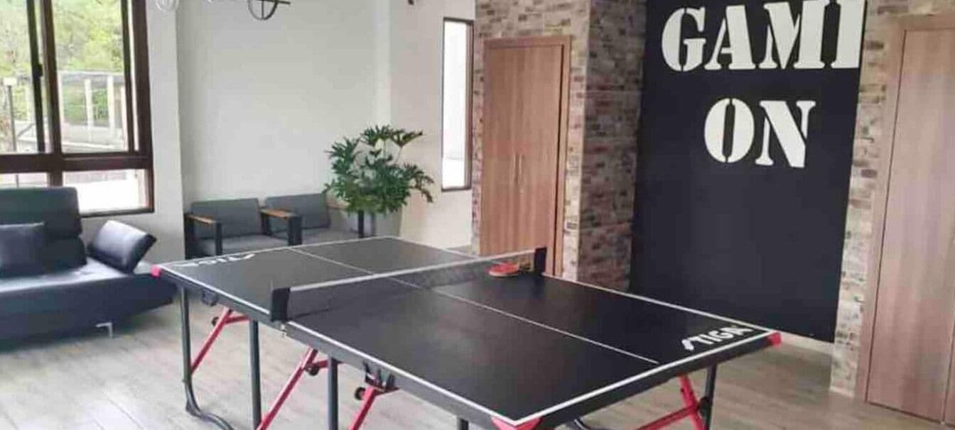 Taula de ping-pong en una habitació amb paret de maó, un sofà i una porta.