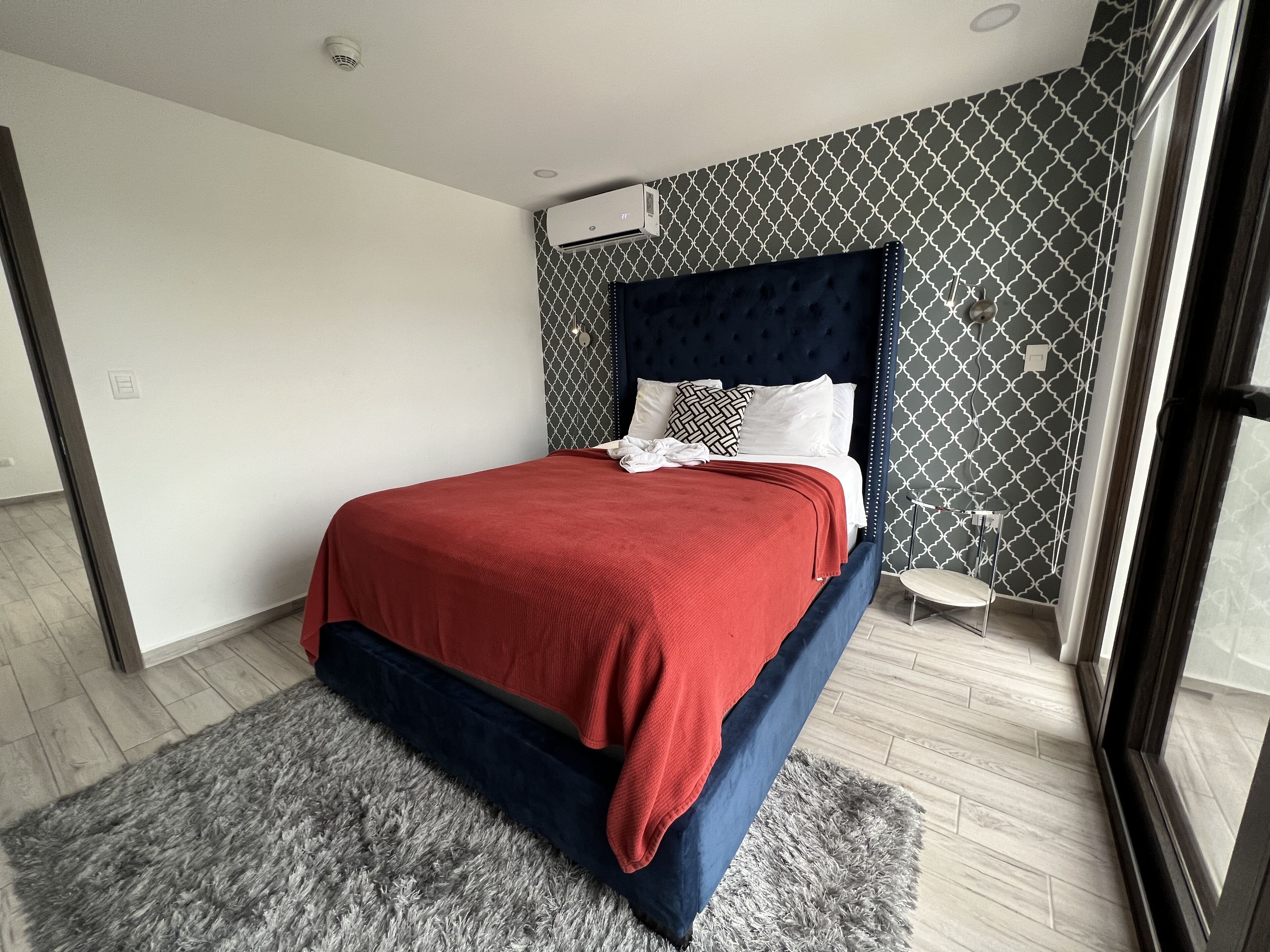 Een moderne slaapkamer met een groot bed, een behang met patroon en een klein nachtkastje.