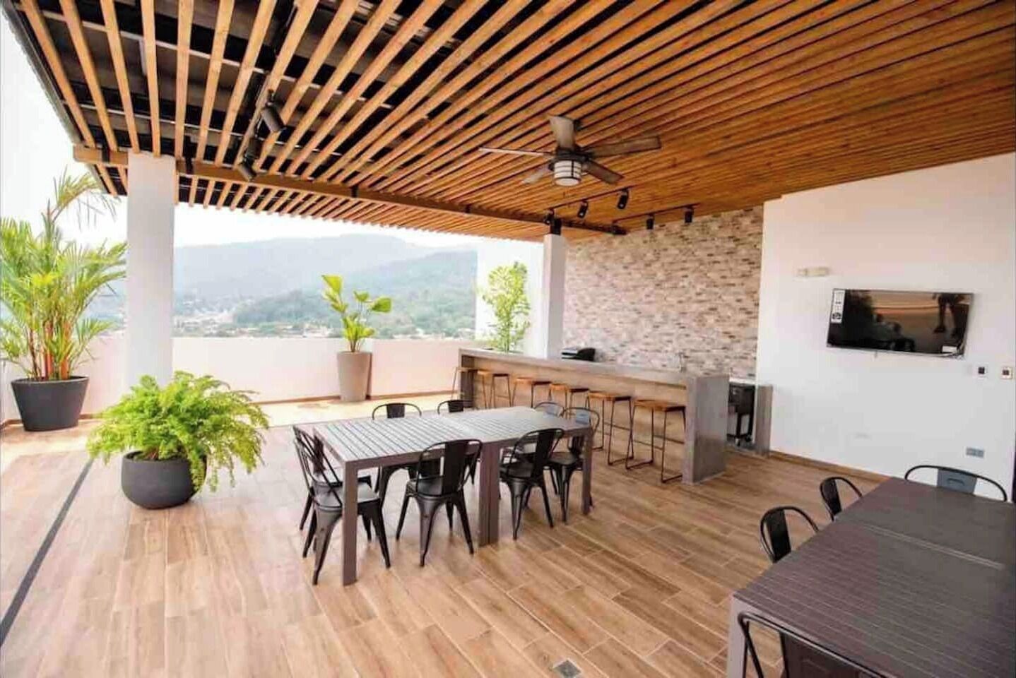 Un espace de restauration extérieur moderne, doté d’un plafond en bois, d’un mur en pierre et d’un téléviseur fixé au mur.