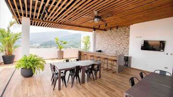 A modern outdoor dining area with a wooden ceiling, a stone wall, and a TV mounted on the wall.