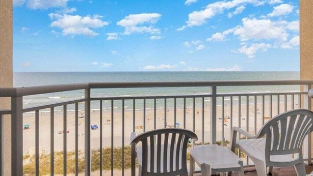 Ein Balkon mit Blick auf einen Strand, ausgestattet mit zwei weißen Plastikstühlen und einem kleinen Tisch.