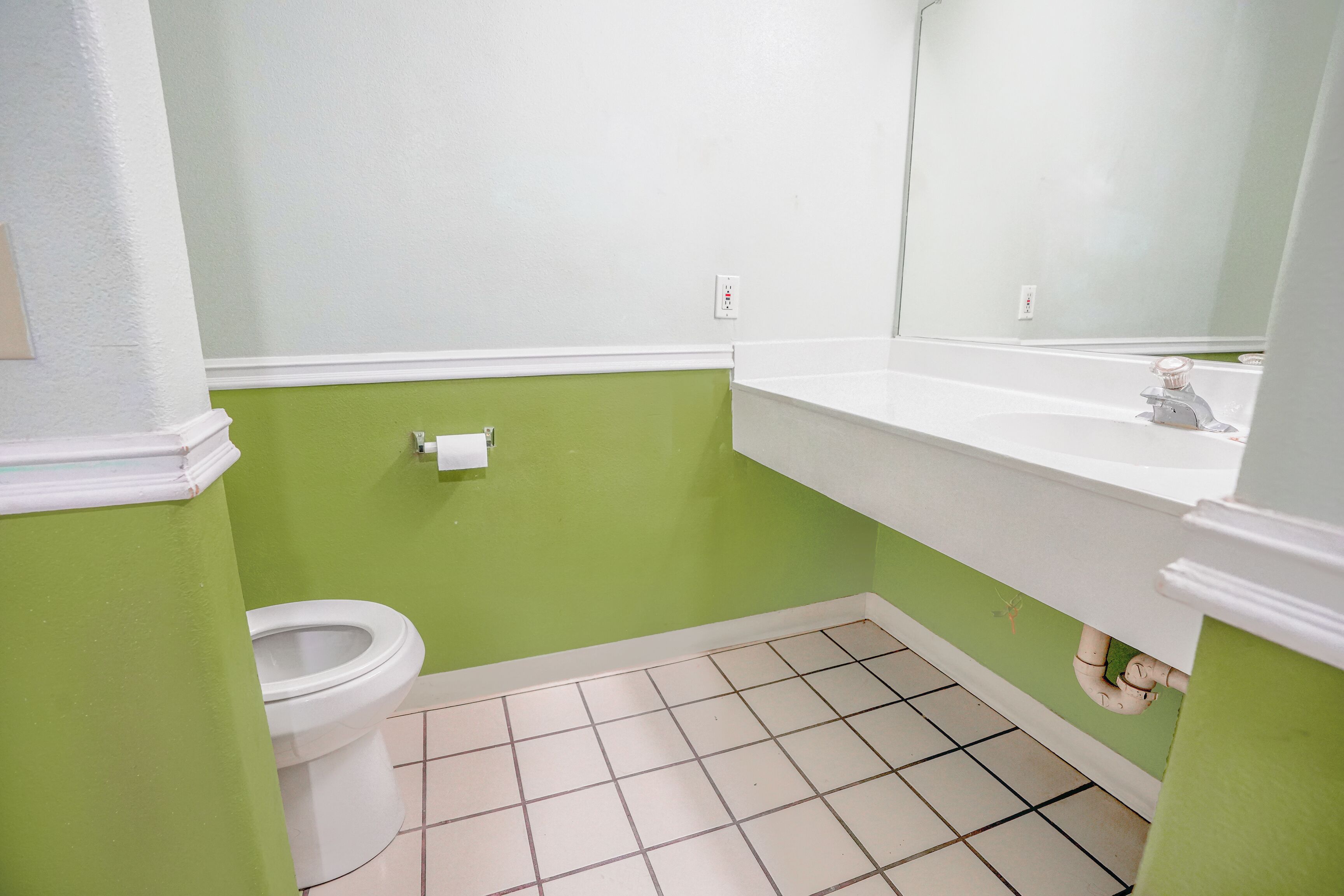 A bathroom with a toilet, sink, and mirror.