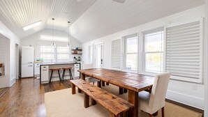 Une cuisine spacieuse avec une table et des bancs en bois, des meubles blancs et de grandes fenêtres.